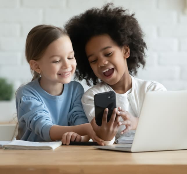 Two children laughing as they learn on a phone